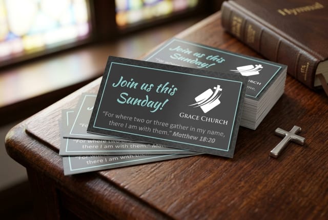 A stack of printed church business cards resting on a wooden table next to a welcome folder and a cup of coffee