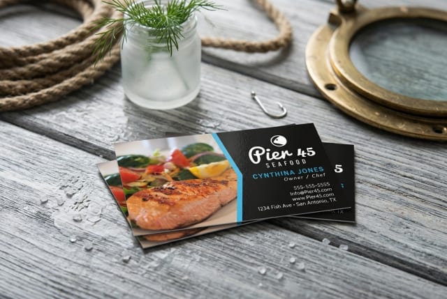 A stack of restaurant business cards sitting on a wooden host stand next to a leather reservation book.