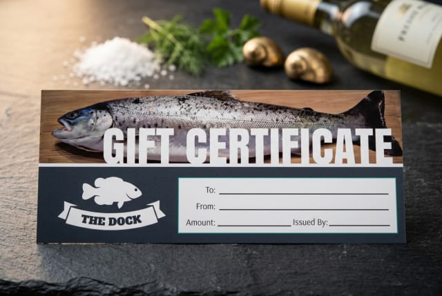 A custom printed restaurant gift certificate resting on a host stand beside a small display of fresh seafood.