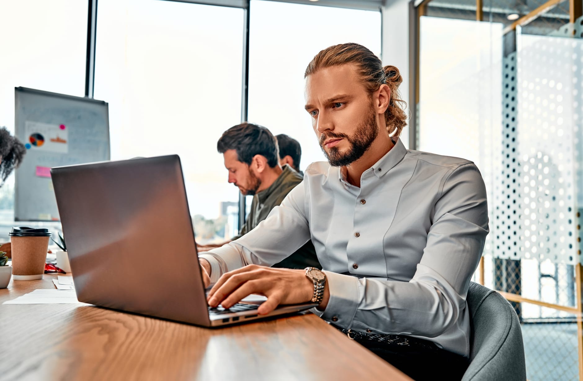 Data analytics. Handsome focused man in stylish shirt working by laptop on background of office with