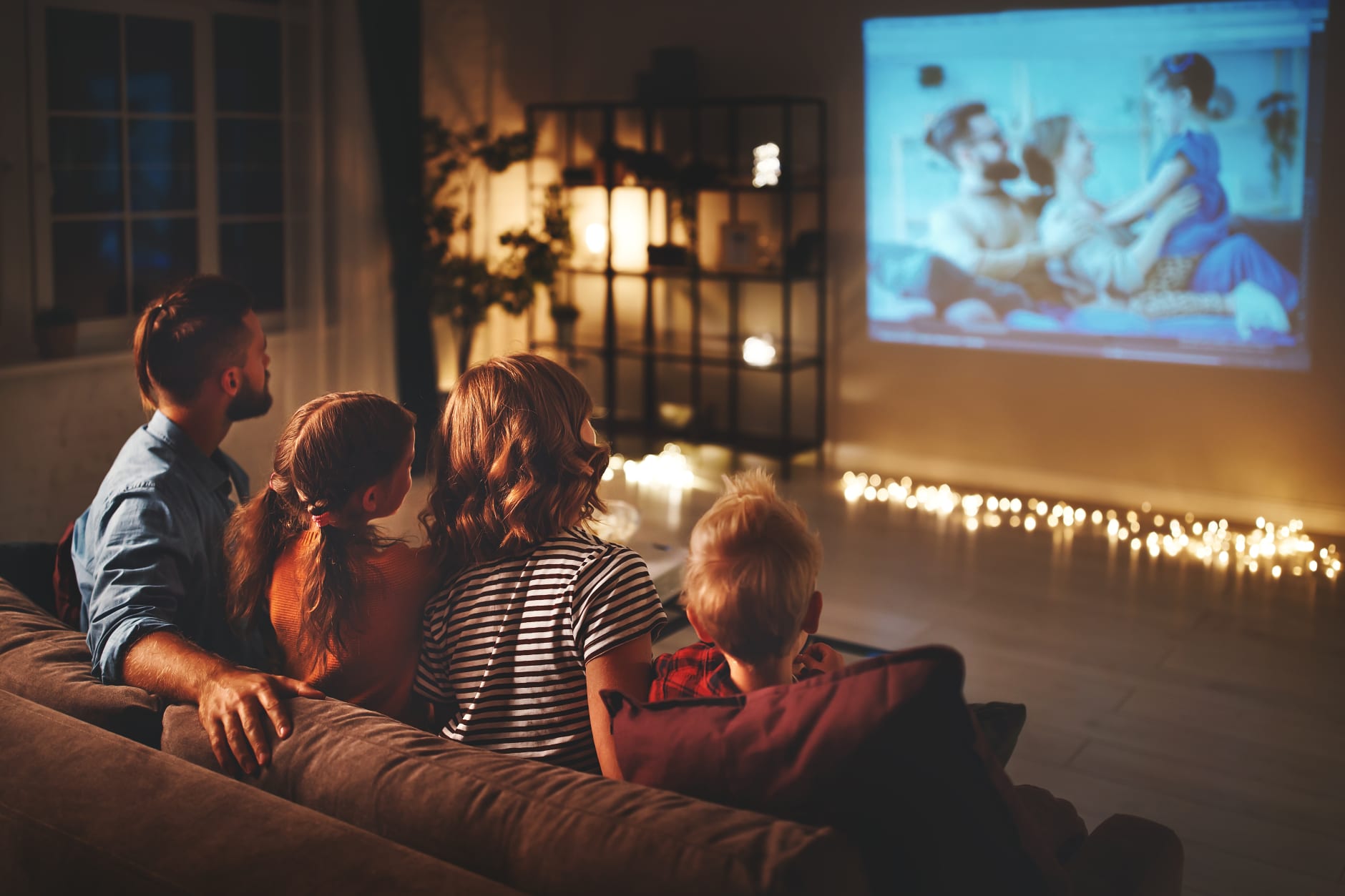 family mother father and children watching projector, tv, movies with popcorn in evening at home