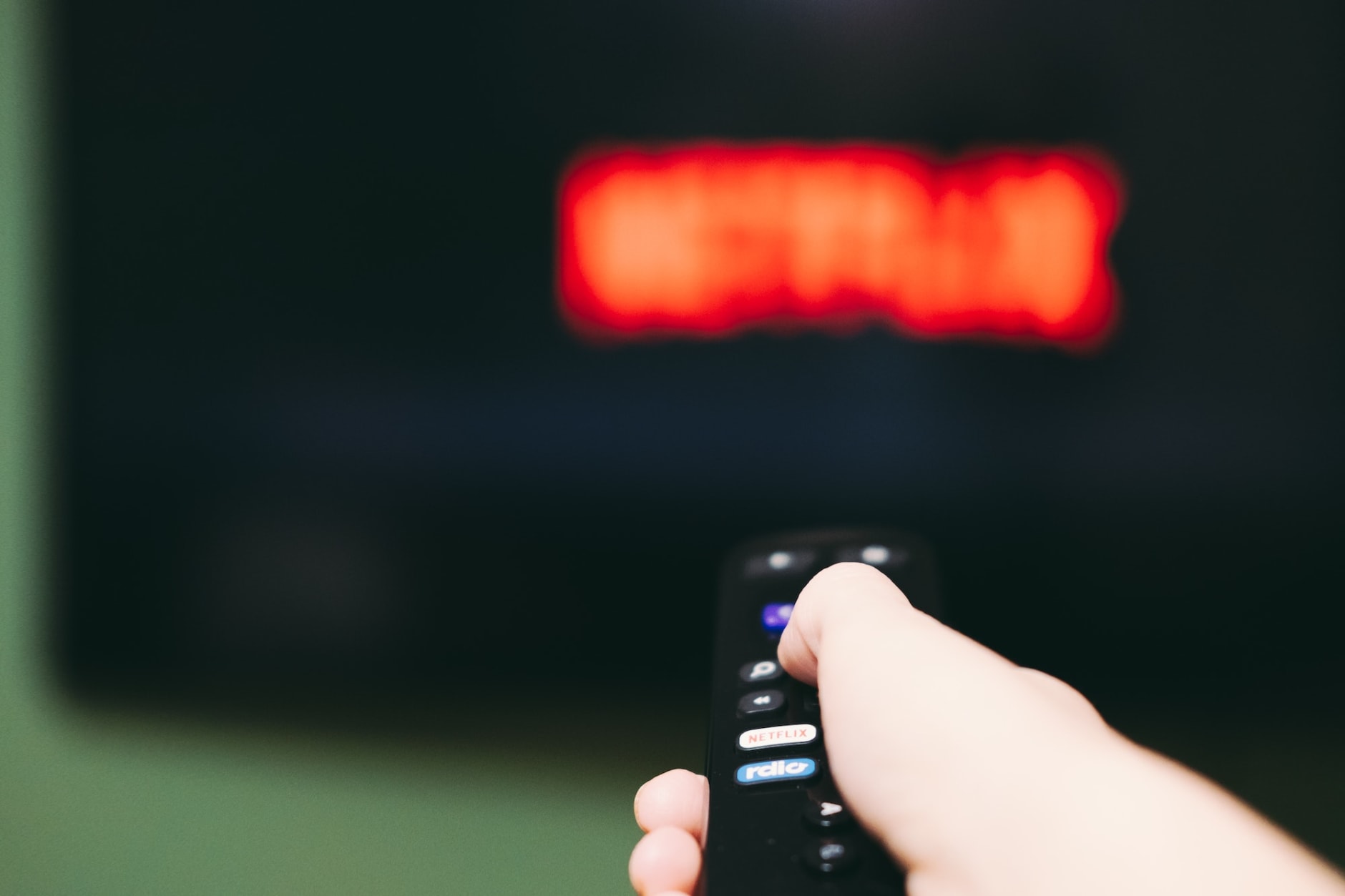 Woman using remote control to switch streaming service on television