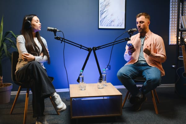 side view of successful woman hosting podcast interviewing man while recording with professional microphones, copy space