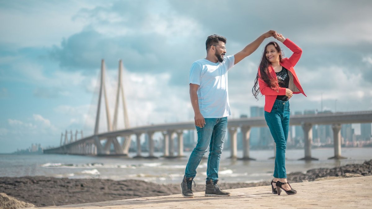 Mumbai waterfront project launches with floating logo display A couple joyously dancing near the iconic Bandra-Worli Sea Link, Mumbai, showcasing love and architecture.