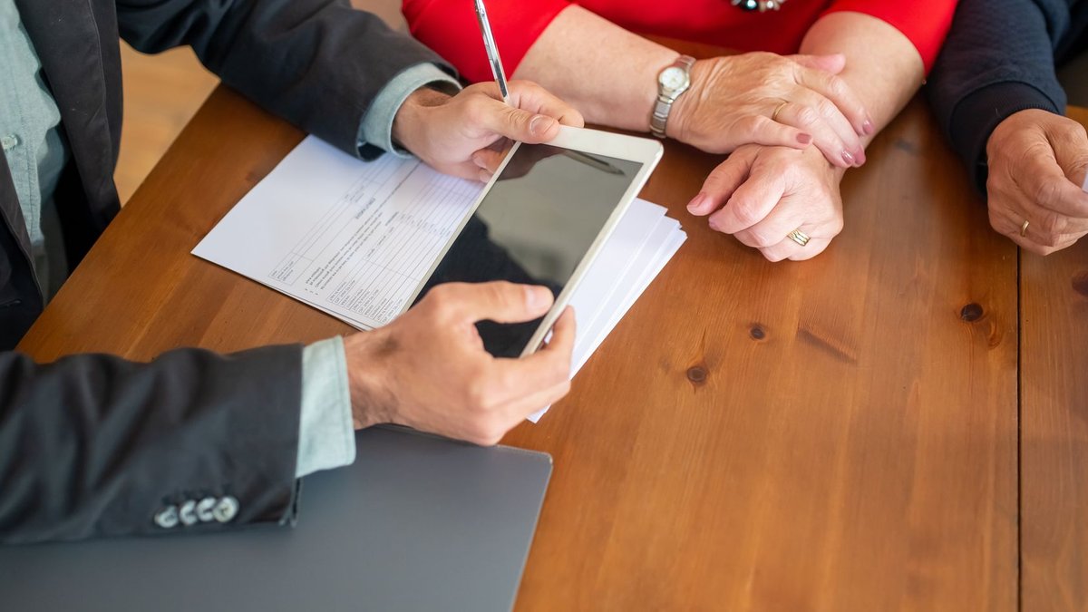 Business meeting at a wooden table with consultant reviewing documents and using a digital tablet.