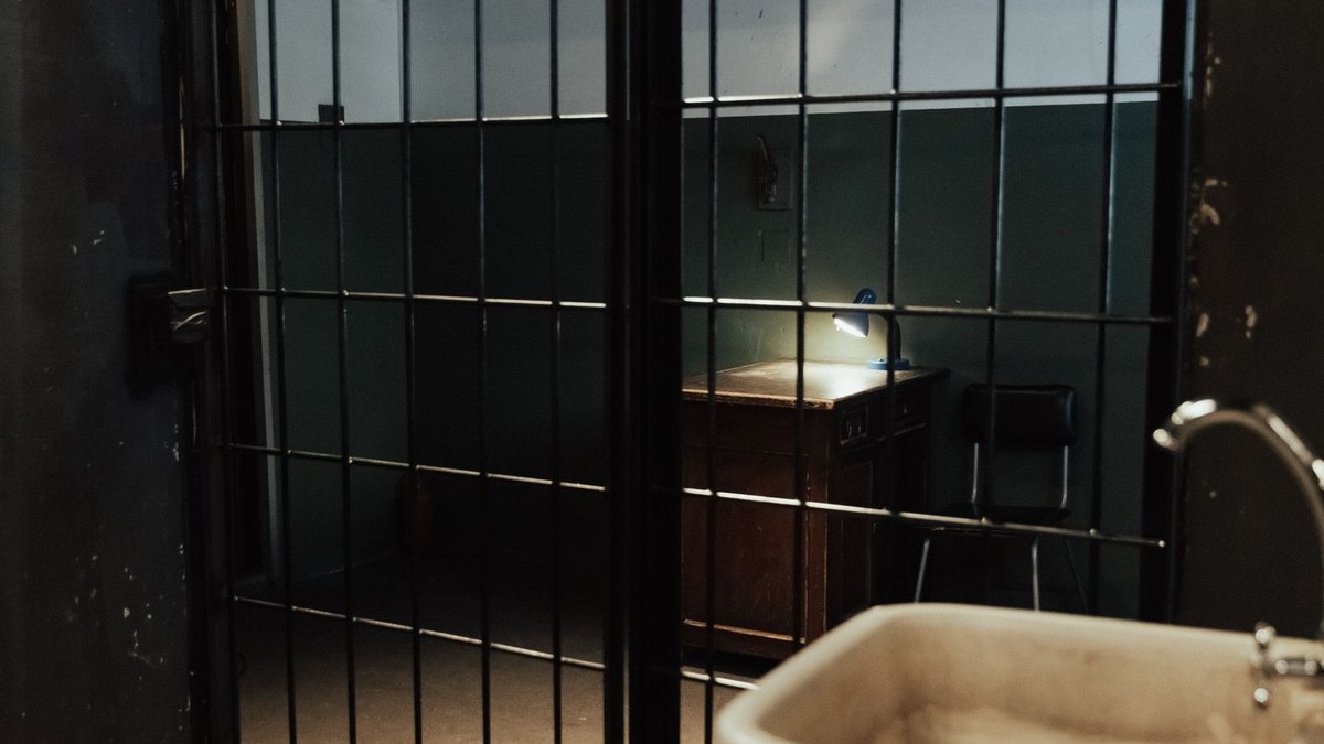 Cellmate Suicide Attempt Raises Concerns for Seafarer Albokhari A dimly lit prison cell interior with metal bars, a sink, and a desk.