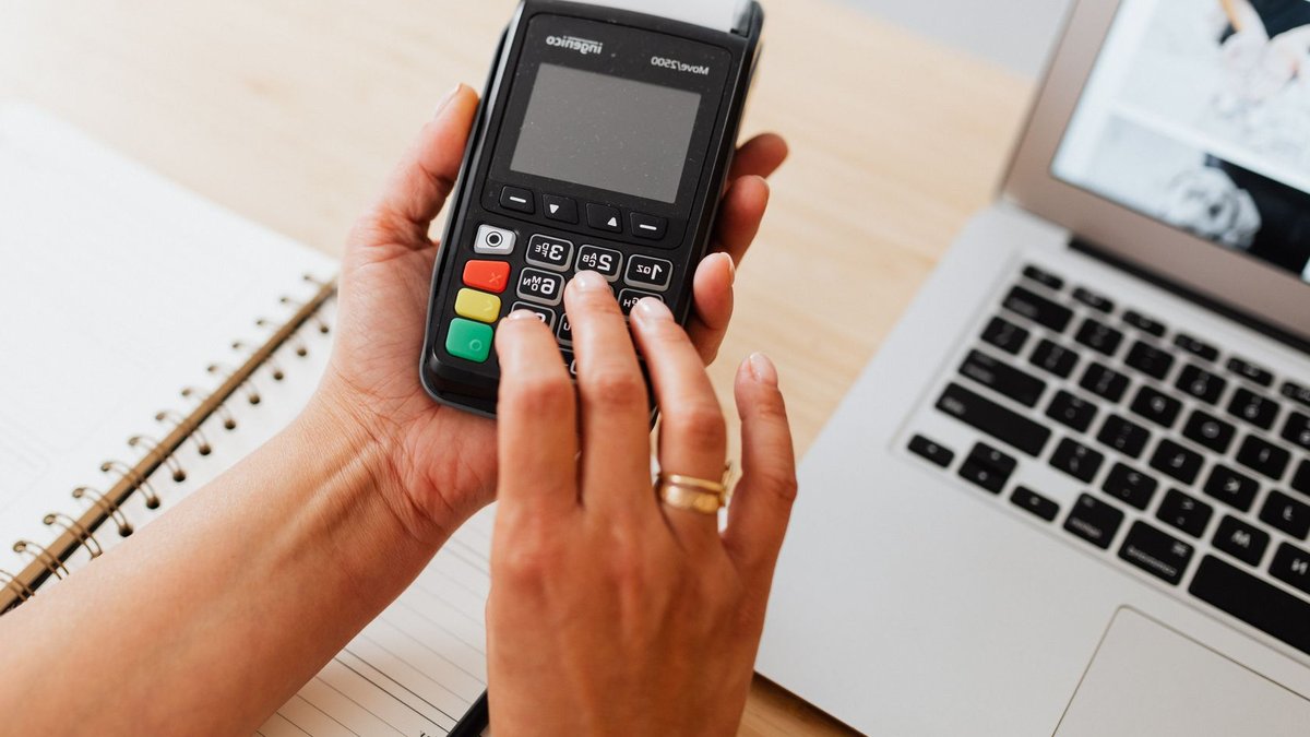Hands using a payment terminal next to a laptop and notebook, showcasing cashless transactions.