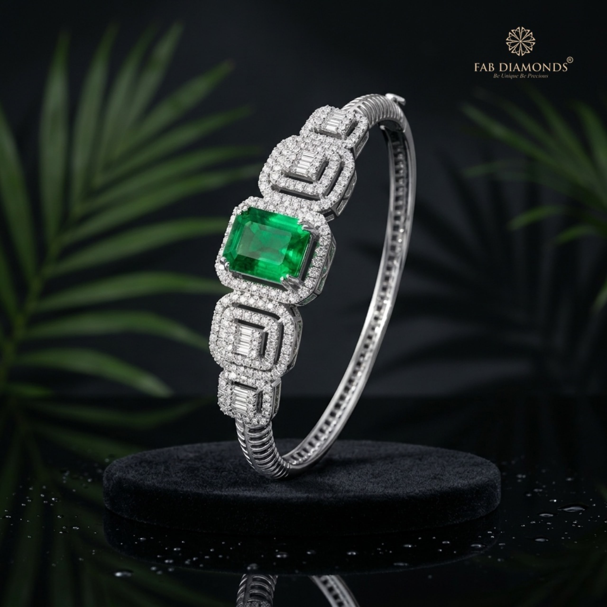 An 18KT white gold hinged bangle with an emerald-cut emerald and four stepped diamond halo stations