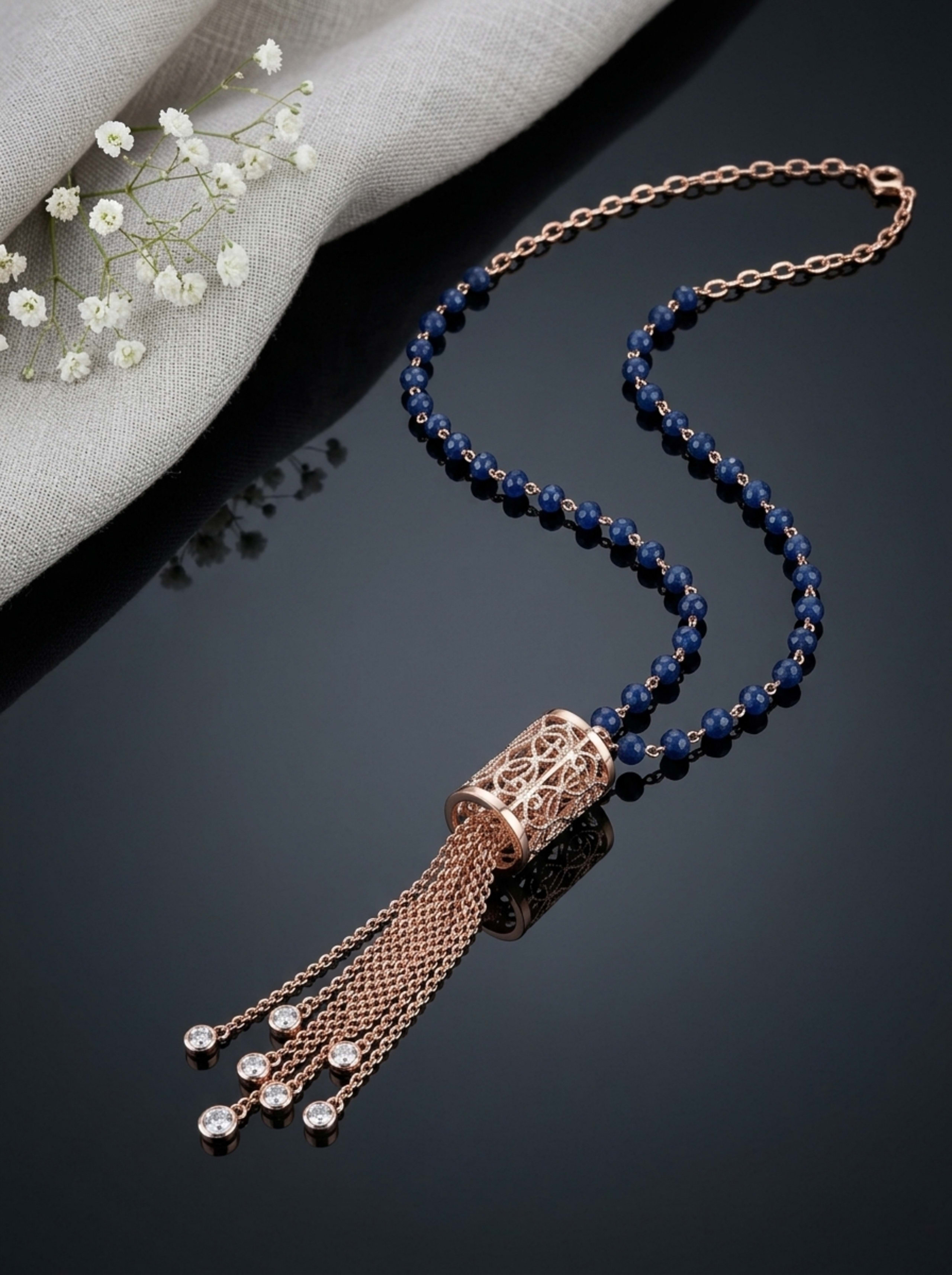 Sapphire Bead and Filigree Barrel Tassel Chain in 18KT rose gold on glossy black surface