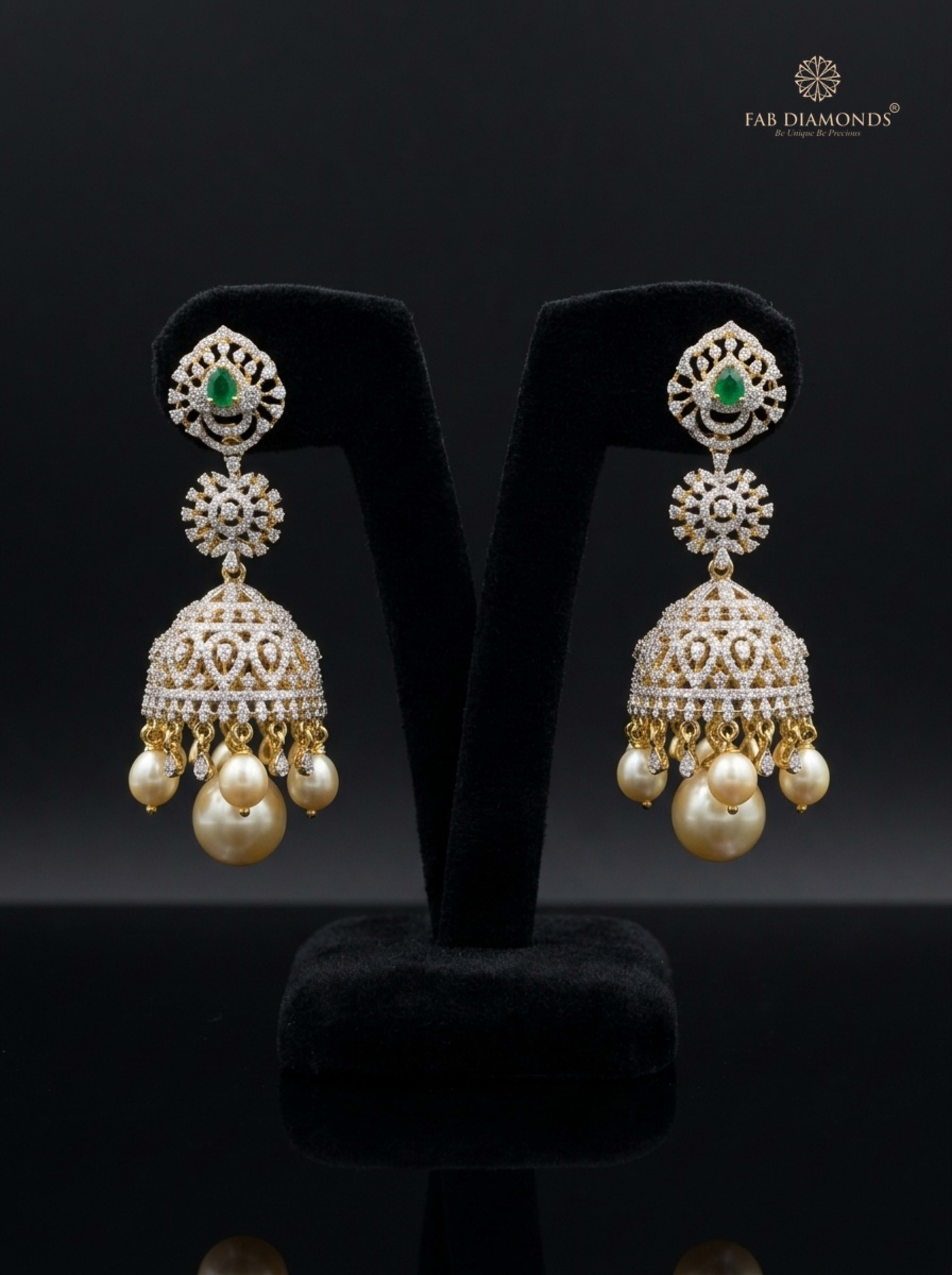 A pair of Saroja tiered diamond jhumkas on matte black background with botanical leaves