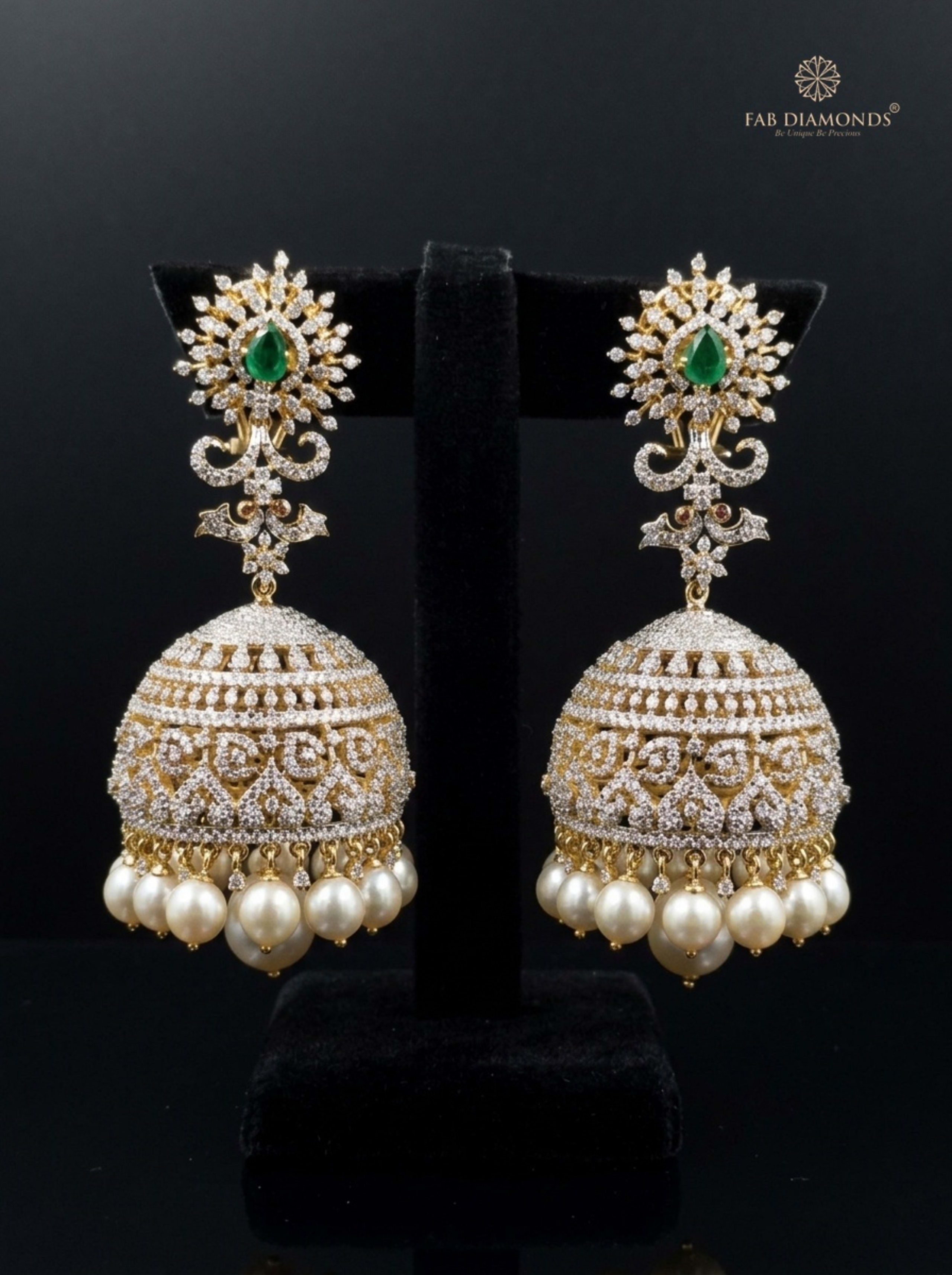 A pair of Ananya grand sunburst emerald and pearl jhumkas on dark rustic wood with rose petals