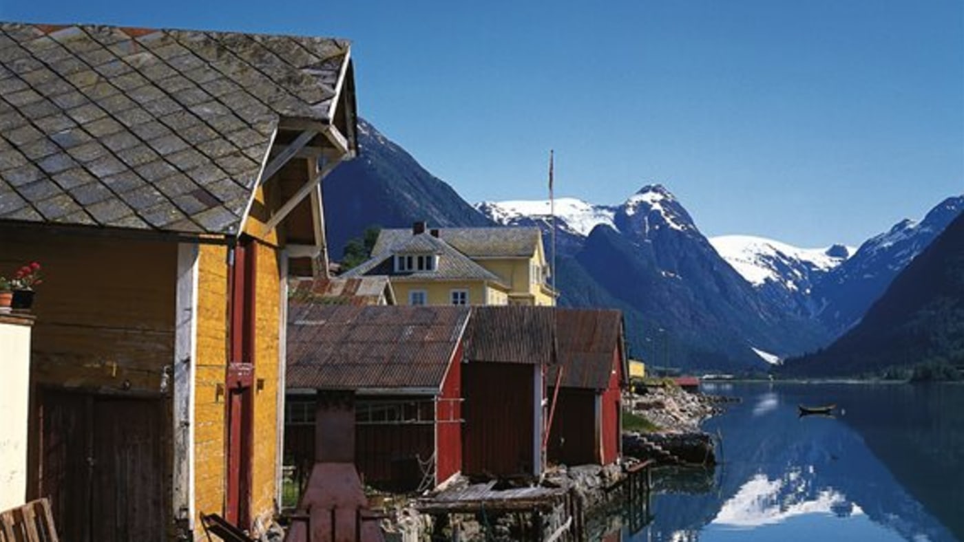 Bygda Fjærland ligg ved foten av Jostedalsbreen, den største breen på det europeiske kontinentet. Gamle hus i vannkanten og snøkledde fjelltopper.