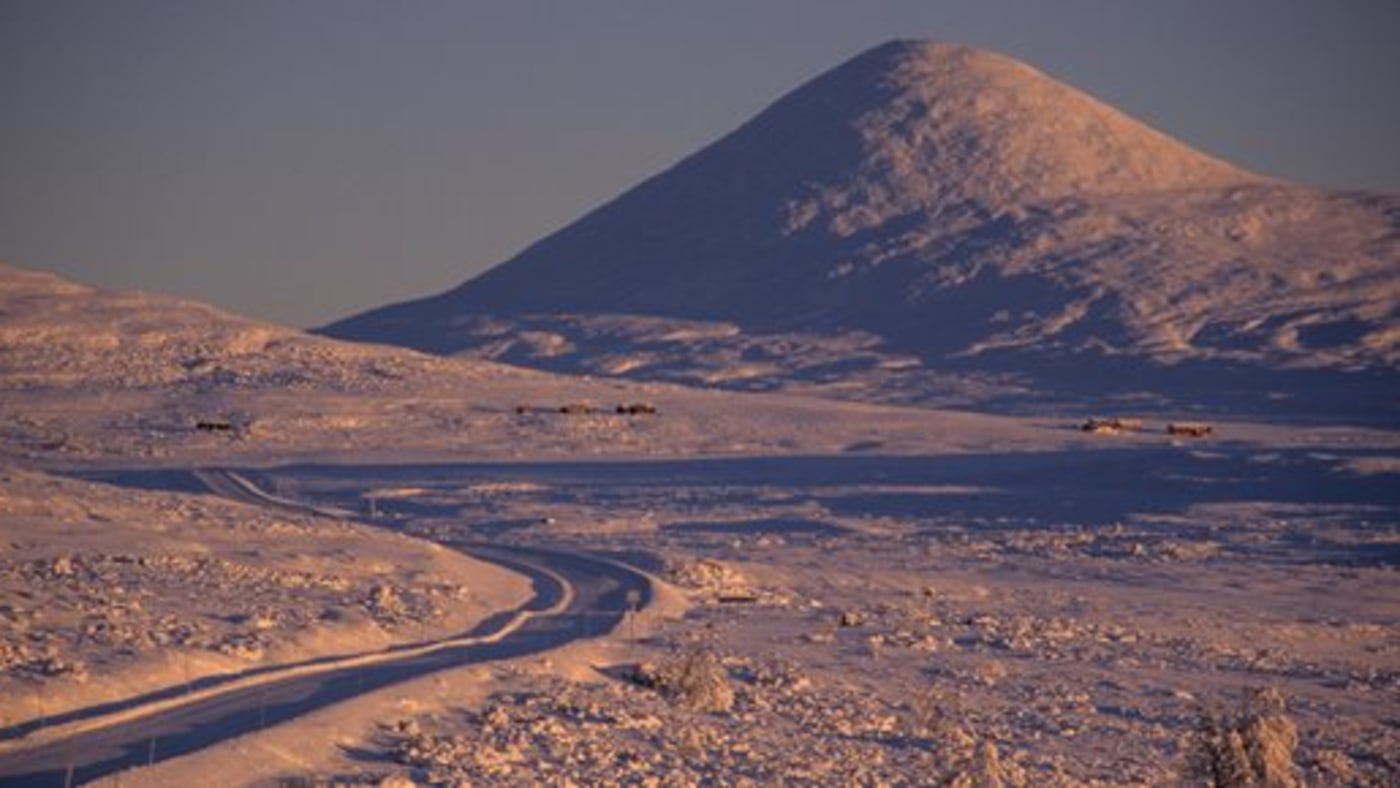 Bilvei gjennom snødekt landskap med fjelltopp. 