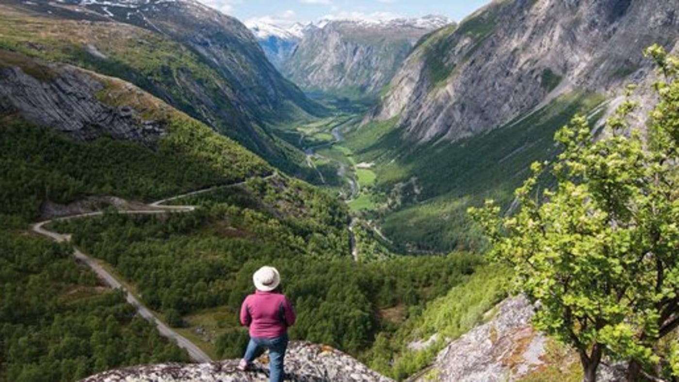 Kvinne titter ut over stupbratt dalføre. 