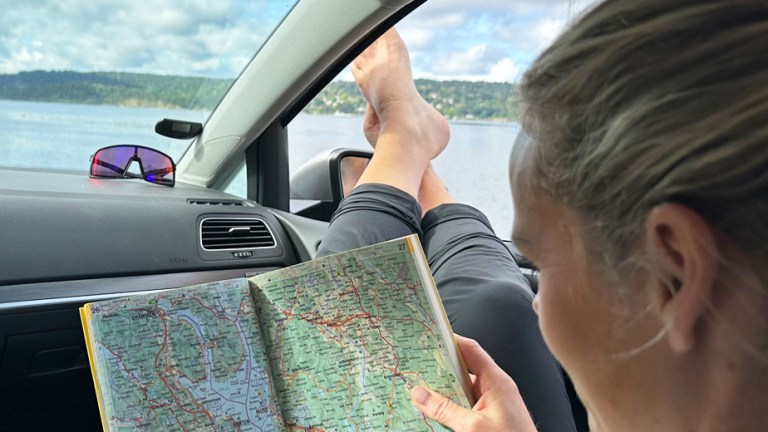 Kvinne sitter i bilen og kikker i NAF Veibok