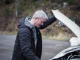 mann sjekker bilbatteriet på hvit bil