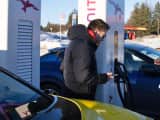 to menn står ved ladestolpe og biler