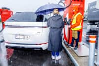 Hvit Xpeng X9 lades i høljregn mens gjennomvåte mennesker ser på