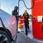 Godt påkledd mann og kvinne står med notatblokk ved siden av en rød Circle K-ladestolpe. Du ser hekken til en Volvo ES90 ved siden av de. 