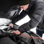 Bildet viser en mann som fester batteriklemmene til startkabler på bilbatteriet sitt.