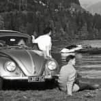 En kvinne og en mann ser ut over en innsjø. Bak dem er en bil parkert.