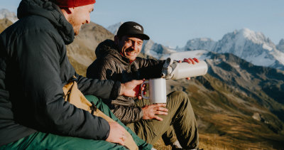To menn sitter i fjellet på høsten og drikker kaffe av CamelBak krus