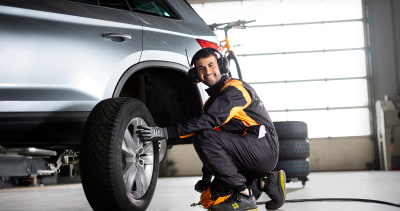 Mann i BestDrive- kjeledress skifter hjul på en bil