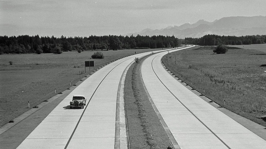 Historisk bilde av en bil som kjører alene på en nybygget motovei