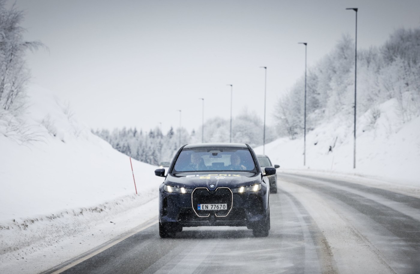Mørk BMW iX på vintervei med snødekte trær rundt. 