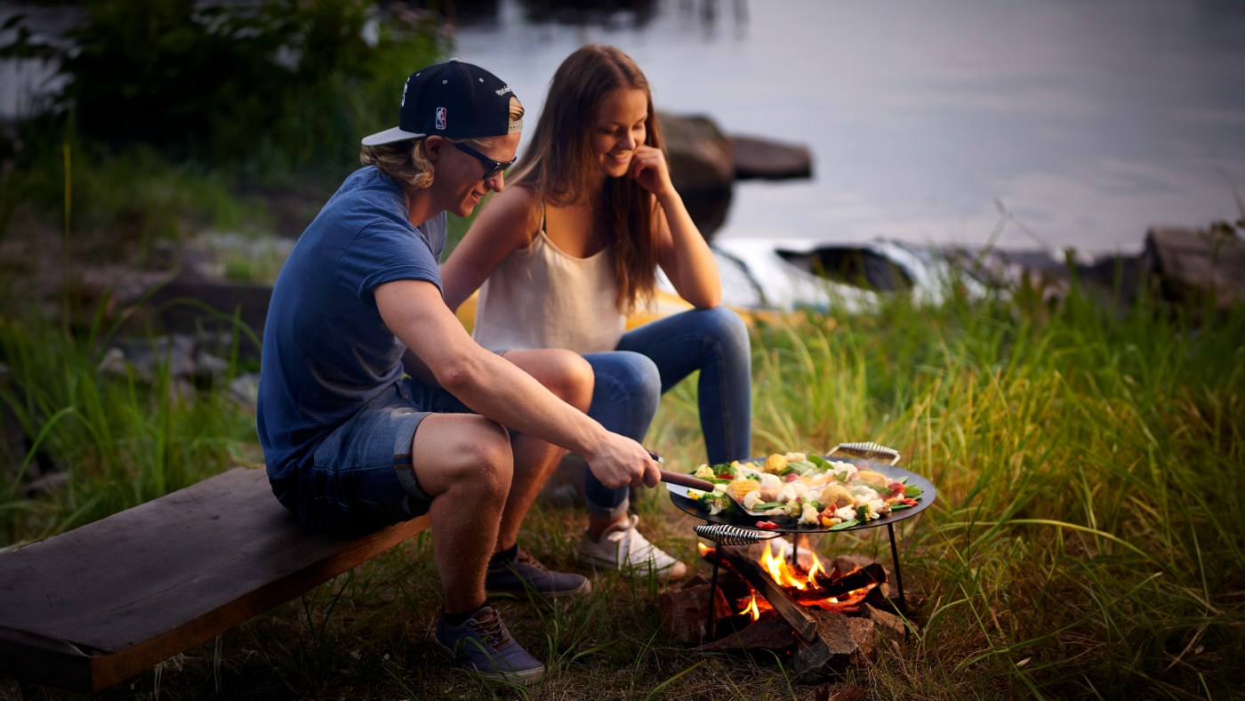 Ungt par som lager mat i friluft ved sjøen en sommerkveld