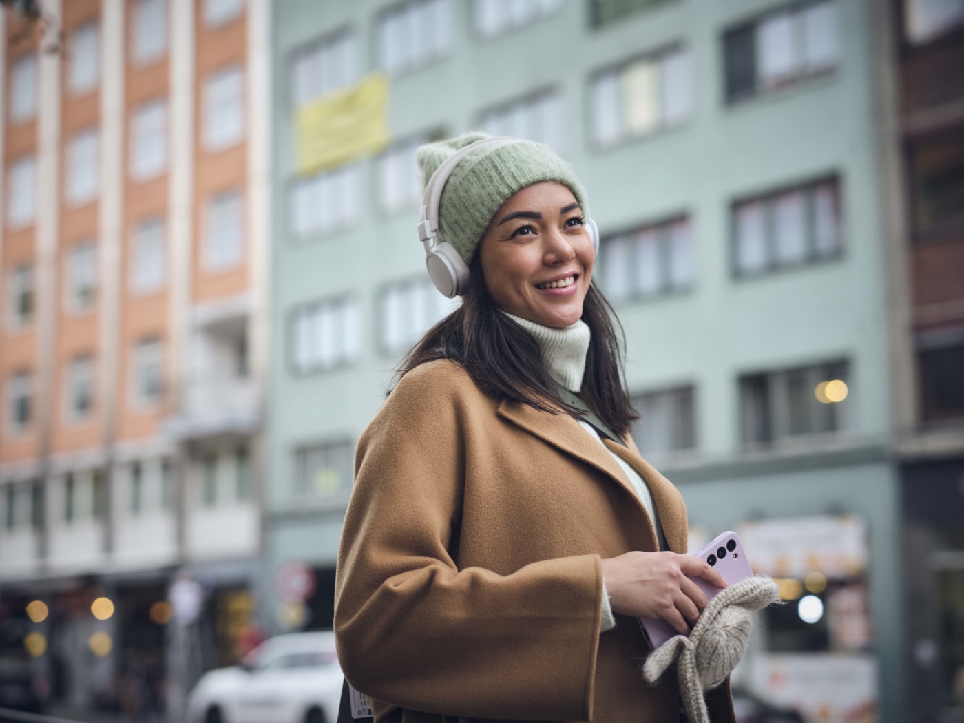 Jente ute på gata i frakk. Lytter til Fabel lydbok