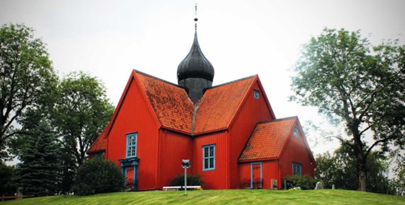 Gammel kirke i tre, med flere utstikkere og spir i midten. 
