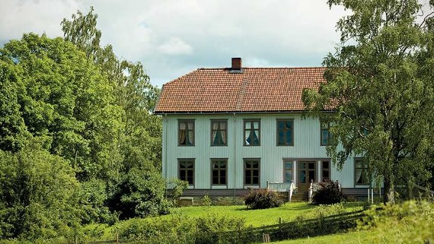 Stort toetasjers hus, omringet av hage og store trær. 