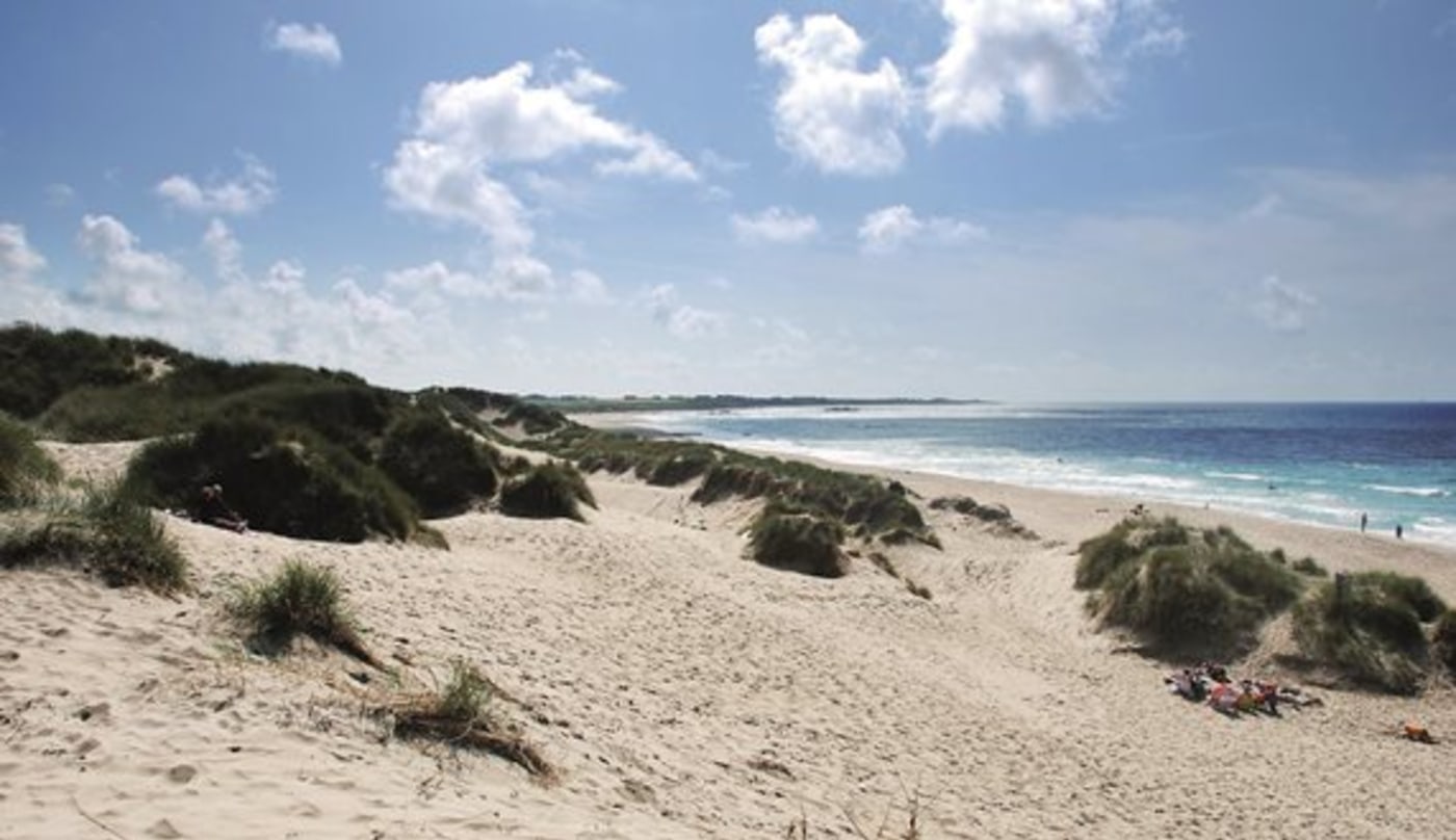 Sandstrand i kuppert terreng med små knauser med gress på.