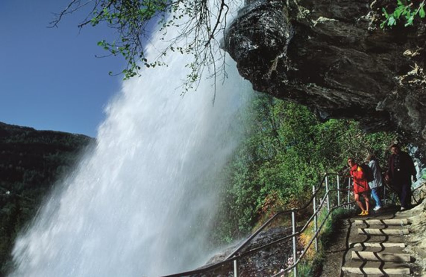 Steindalsfossen med turister på utsiktspunktet, bak fossen. 