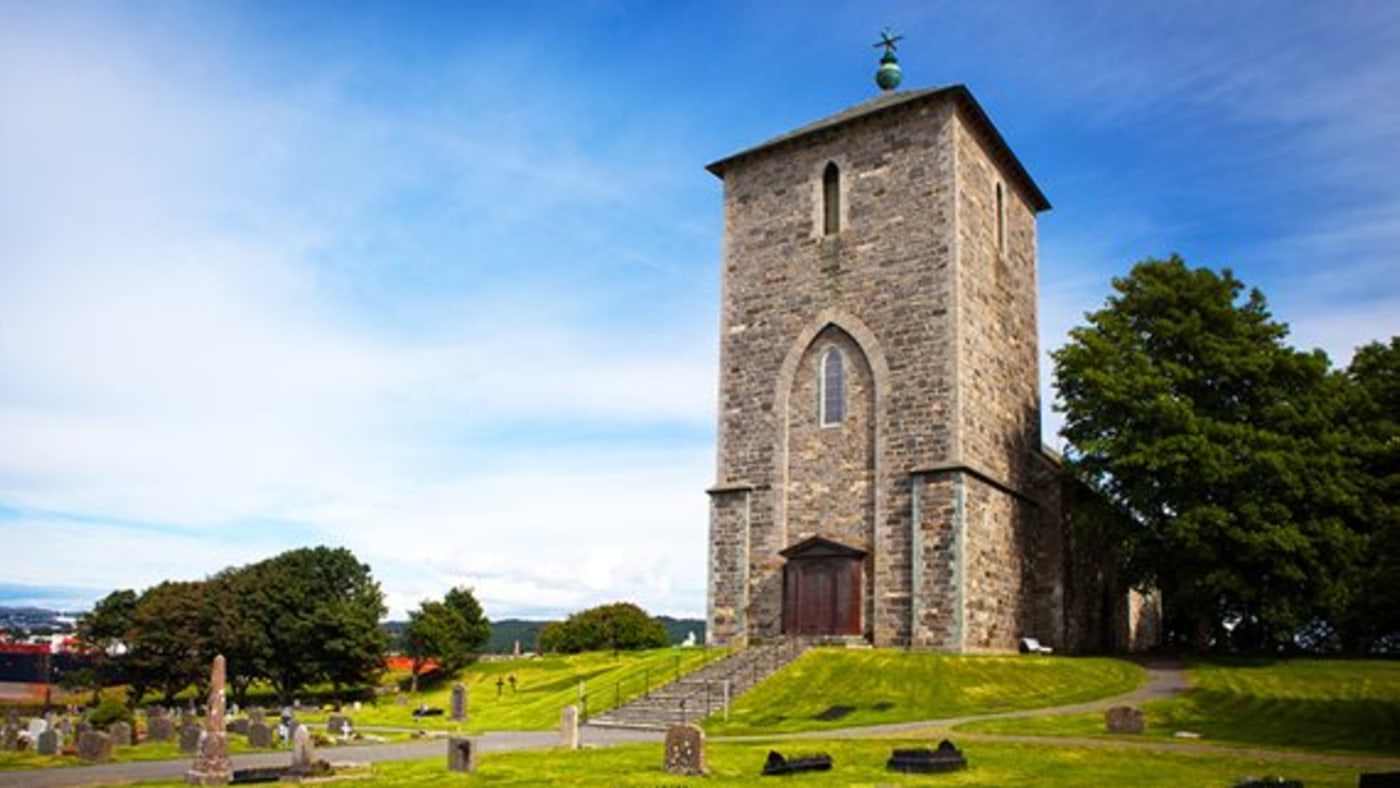 Avaldsnes kirke, bygget i stein. Høyt inngangsparti med trapp i skråning, i front. 
