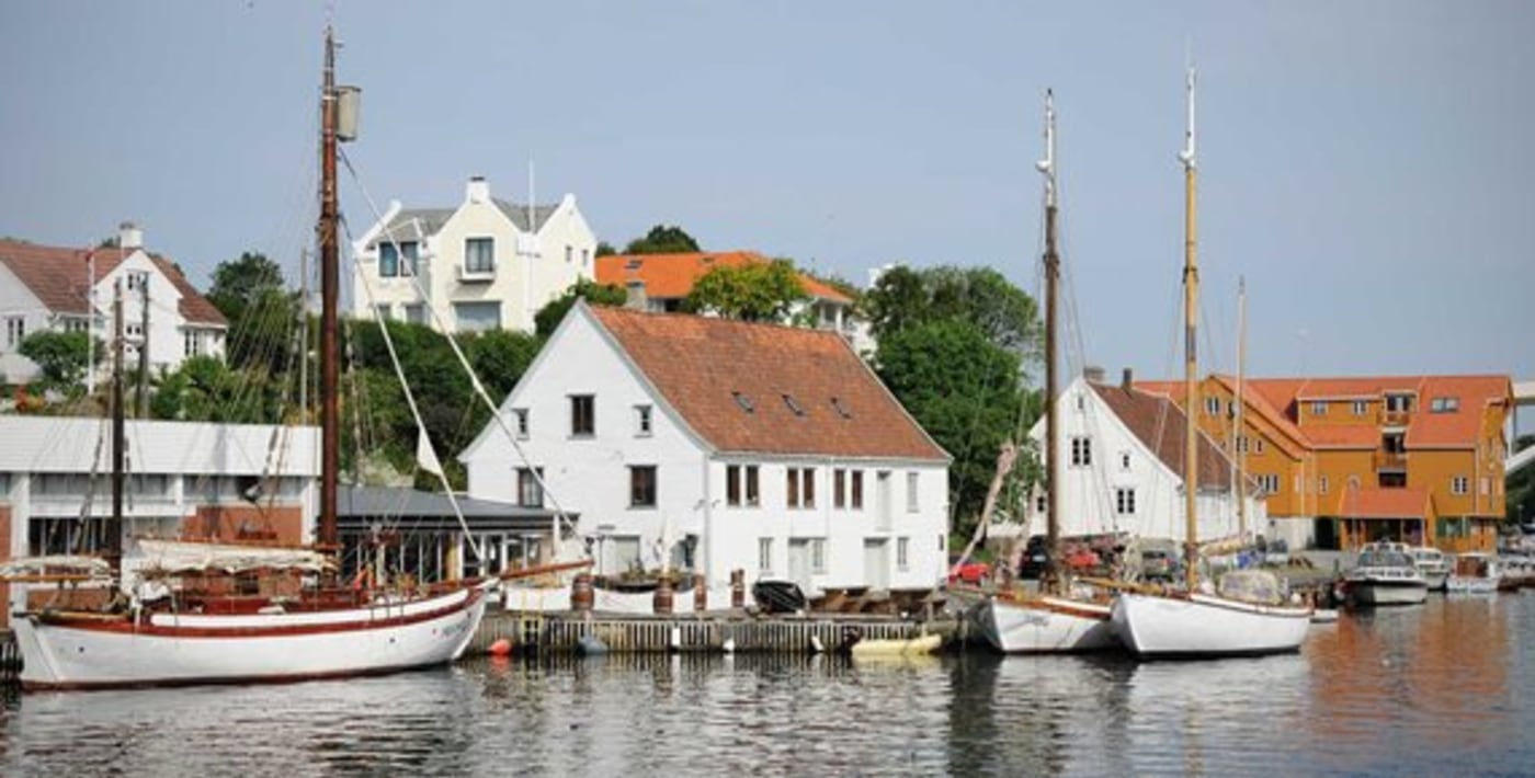Seilbåter ligger inntil brygge med gamle trehus langs havna. 