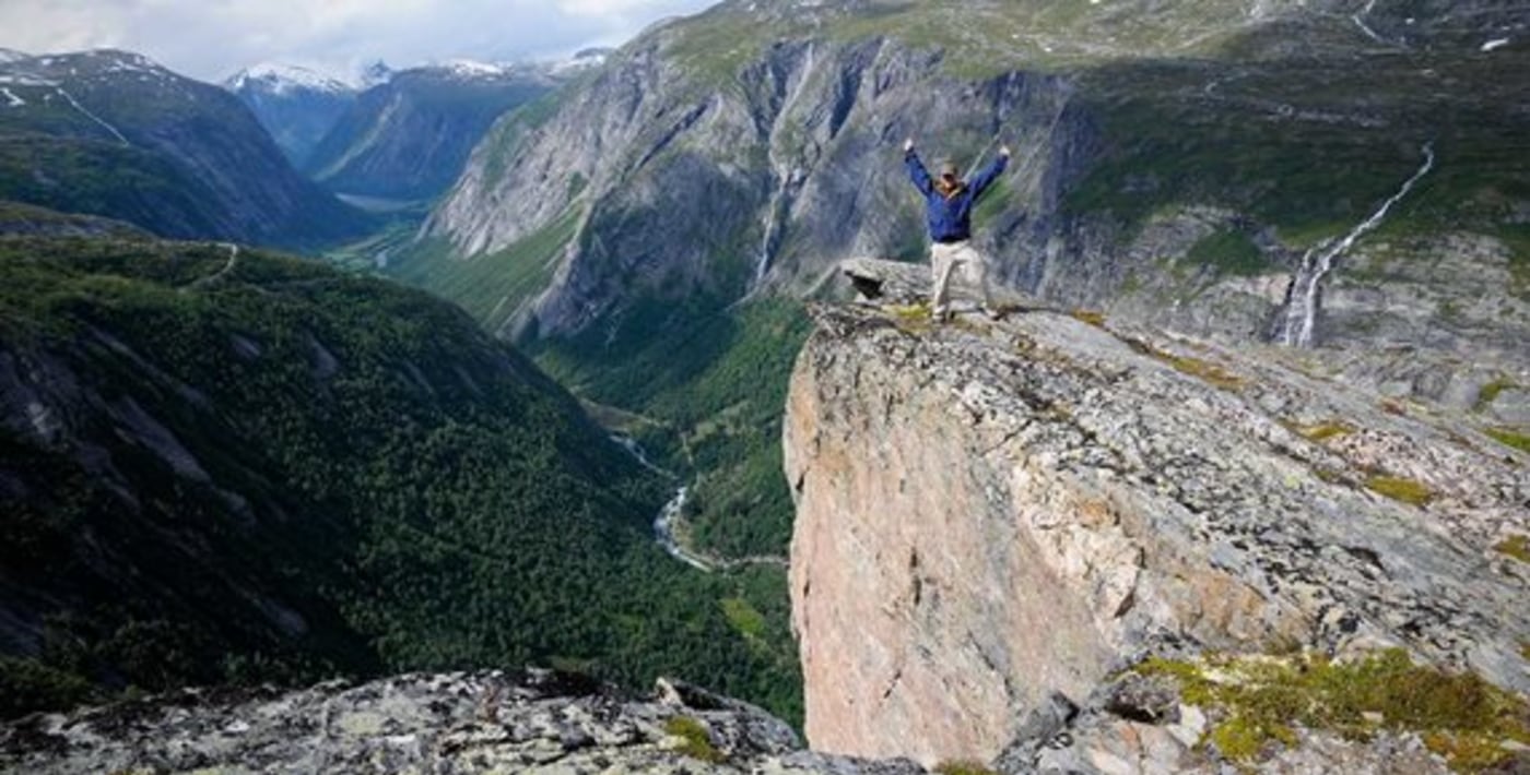 Mann står på tuppen av et stup med langstrakt dalføre i bakgrunnen. 