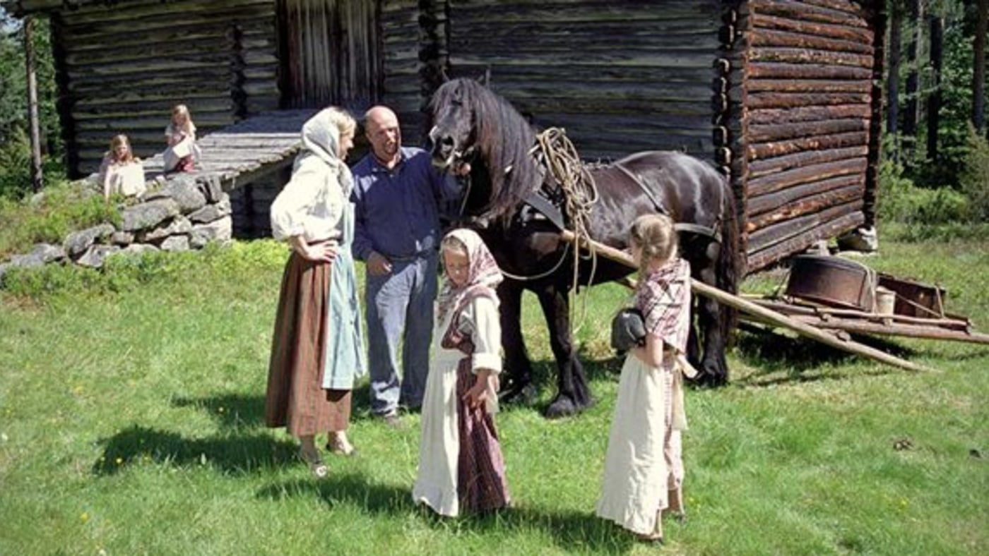 Mann, dame og barn. Kledd ut som gammel gårdsfamilie. Hest og lafta hus. 
