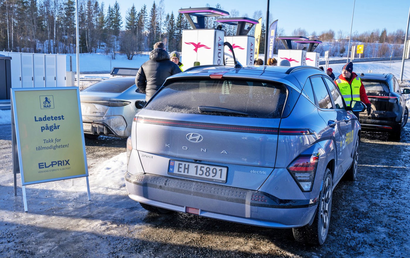 Elbil ved hurtigladestasjon. Skilt med teksten "ladetest pågår" står ved siden av bilen