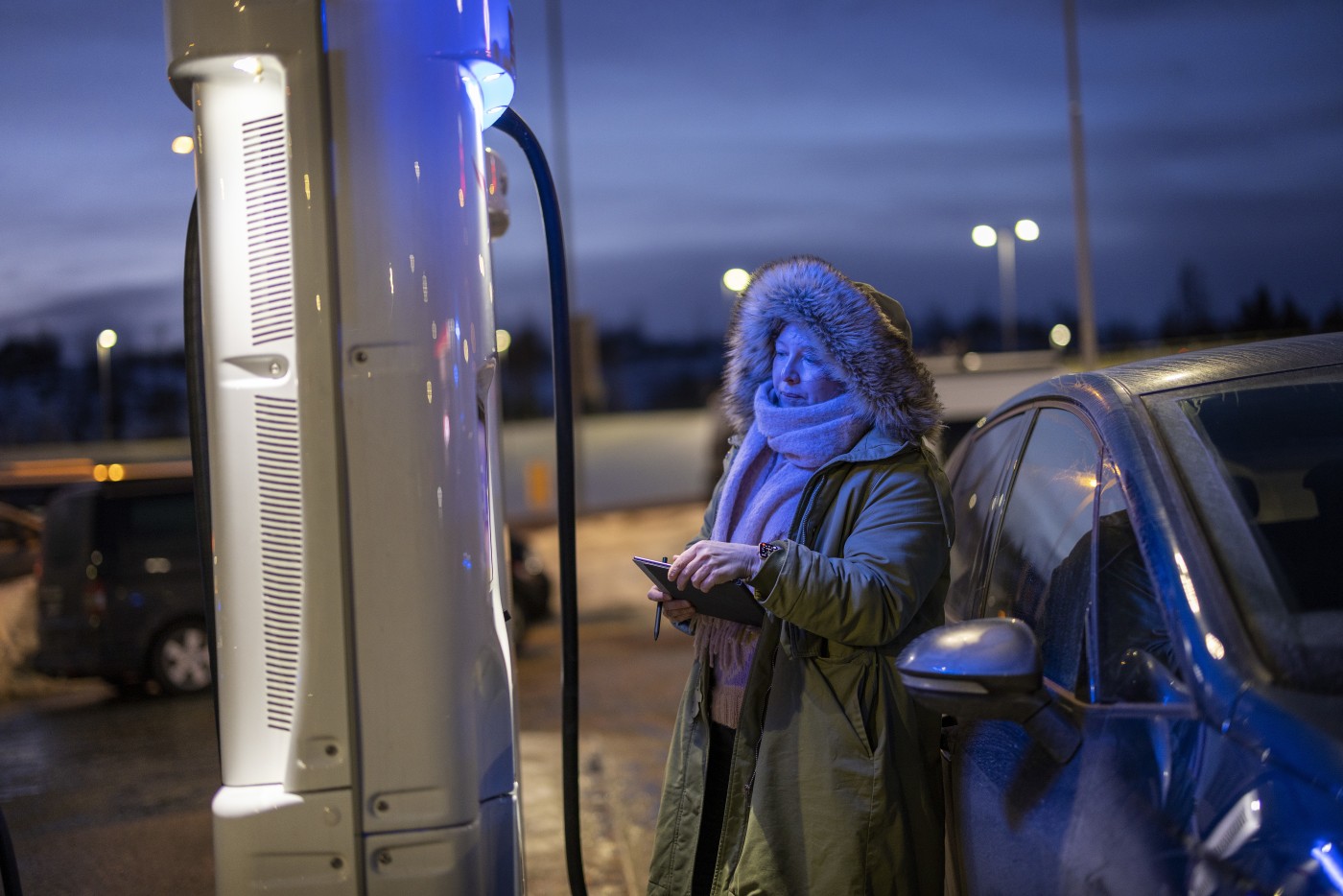 Dame lader elbilen på ladestasjon