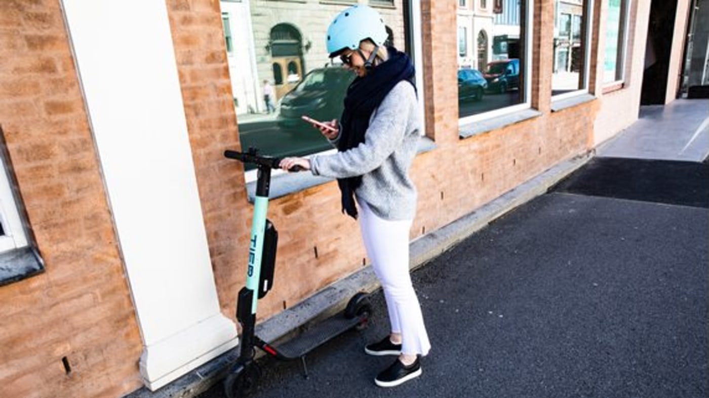 Bildet iser en dame som låser opp en elsparkesykkel med mobilappen.