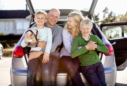 Familie sitter i åpent bagasjerom til forsikret bil.