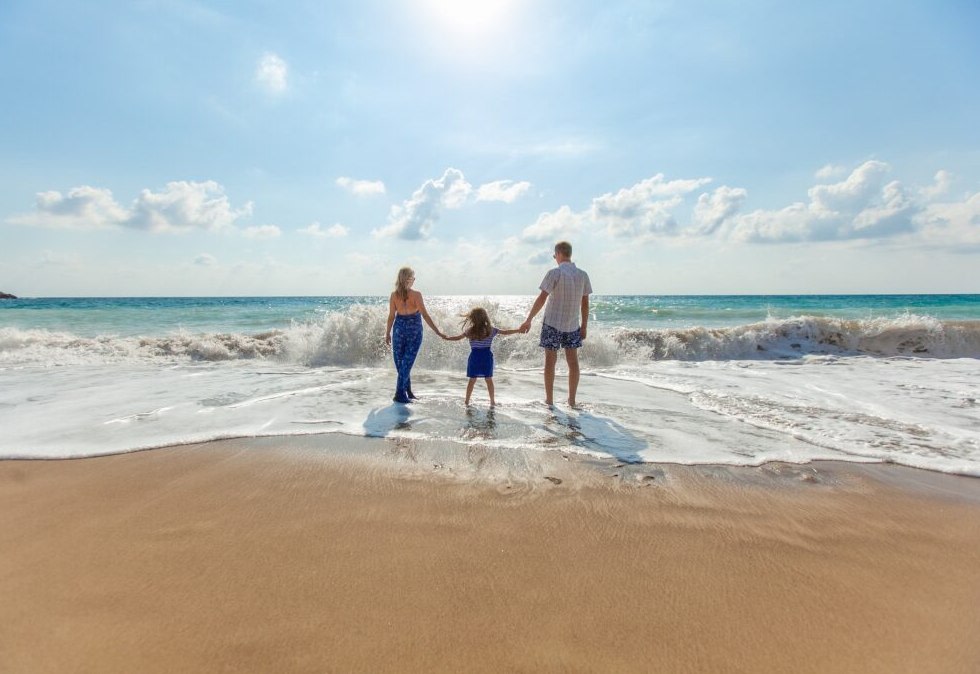 Familie i vannkanten på stranden i ferien