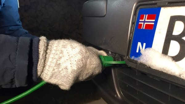 Bildet viser en mann som fester en elektrisk motorvarmer på bilen.