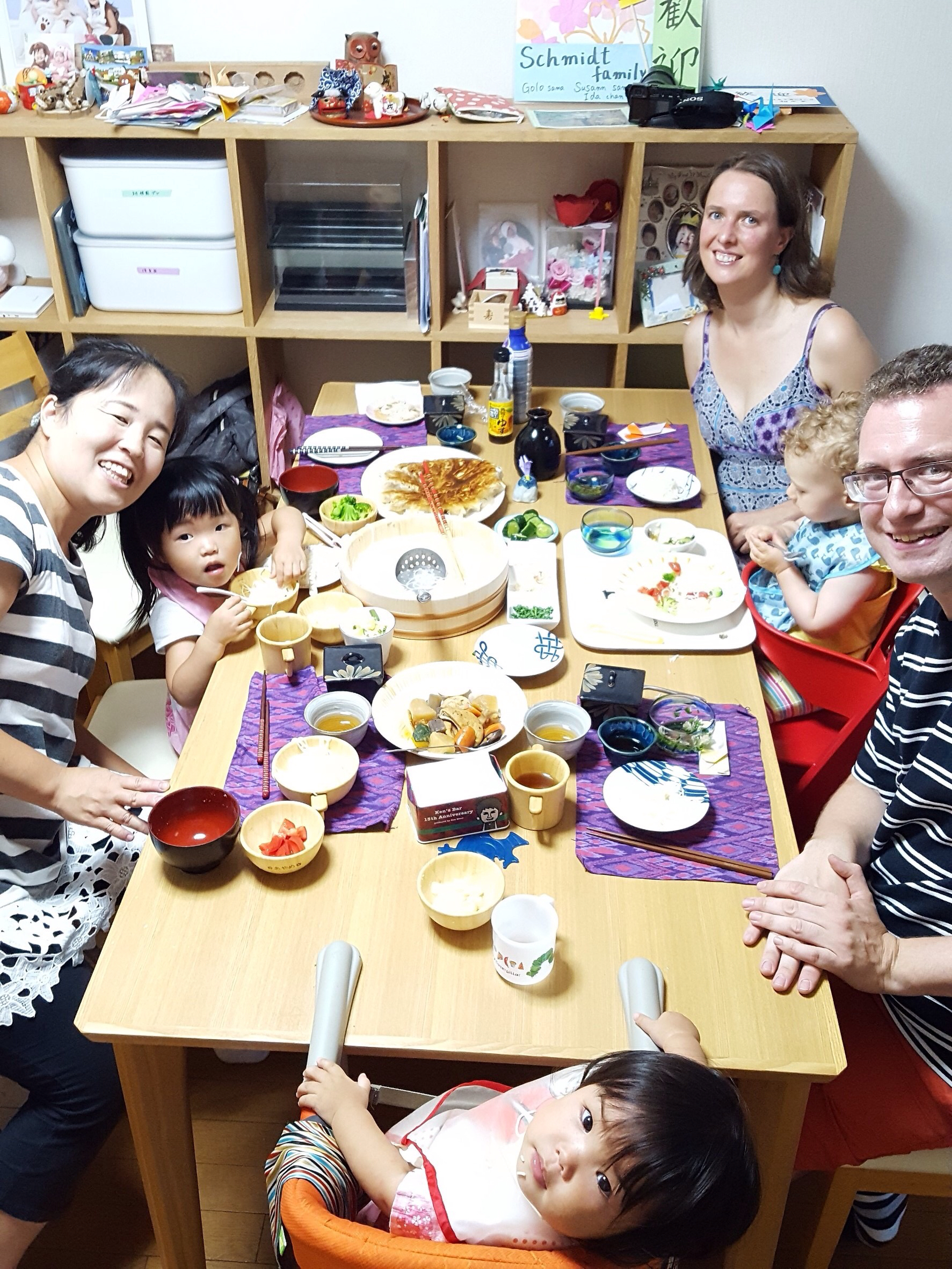 A family gathers at a dining table with many small dishes and a high chair.
