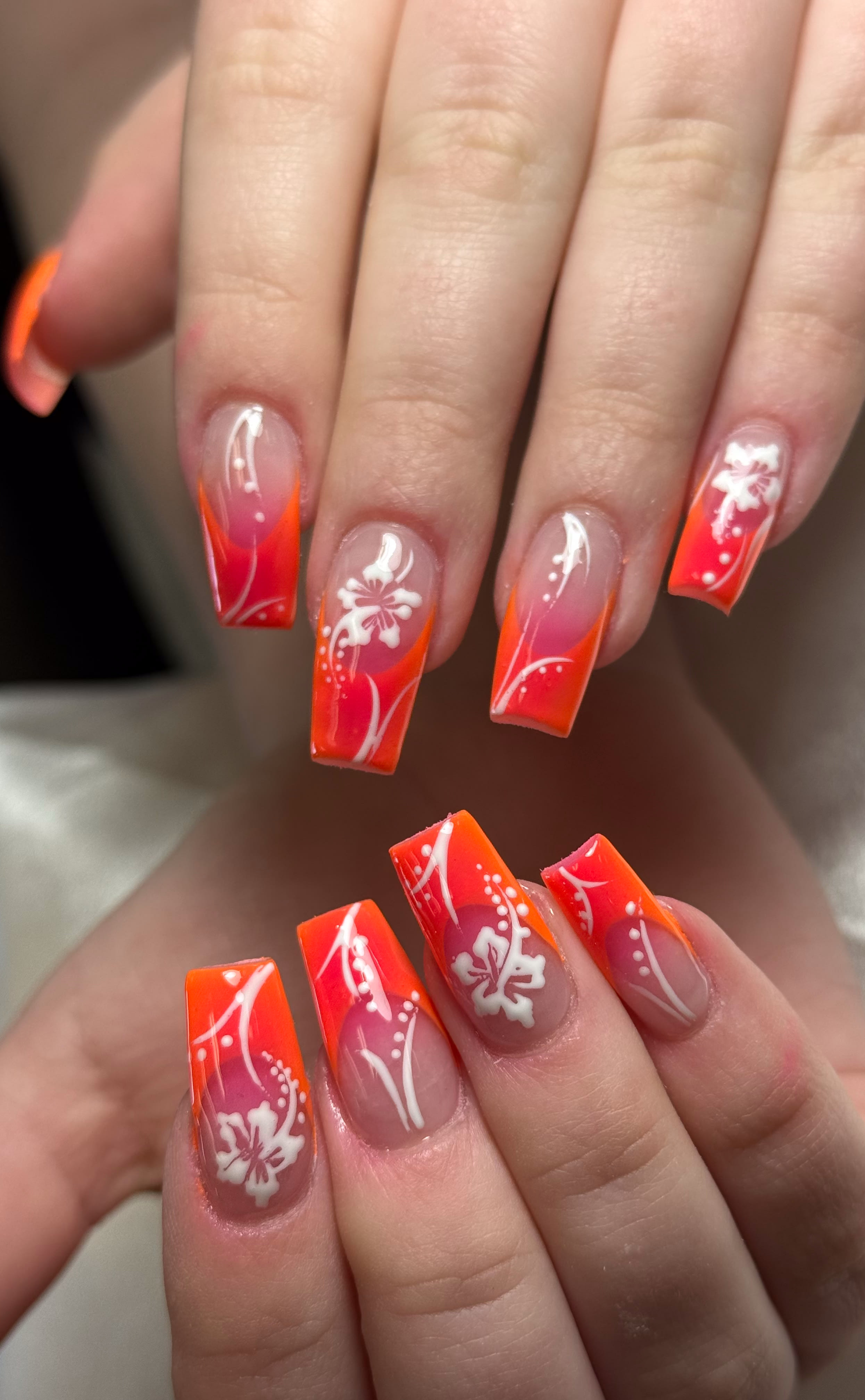 Bright orange and pink nails with white floral art.