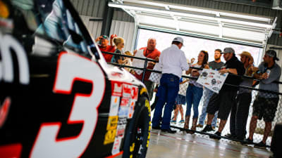 Team owner Richard Childress signs autographs for fans in front of Dale Earnhardt's No. 3 Chevrolet in the Talladega Superspeedway garage area.