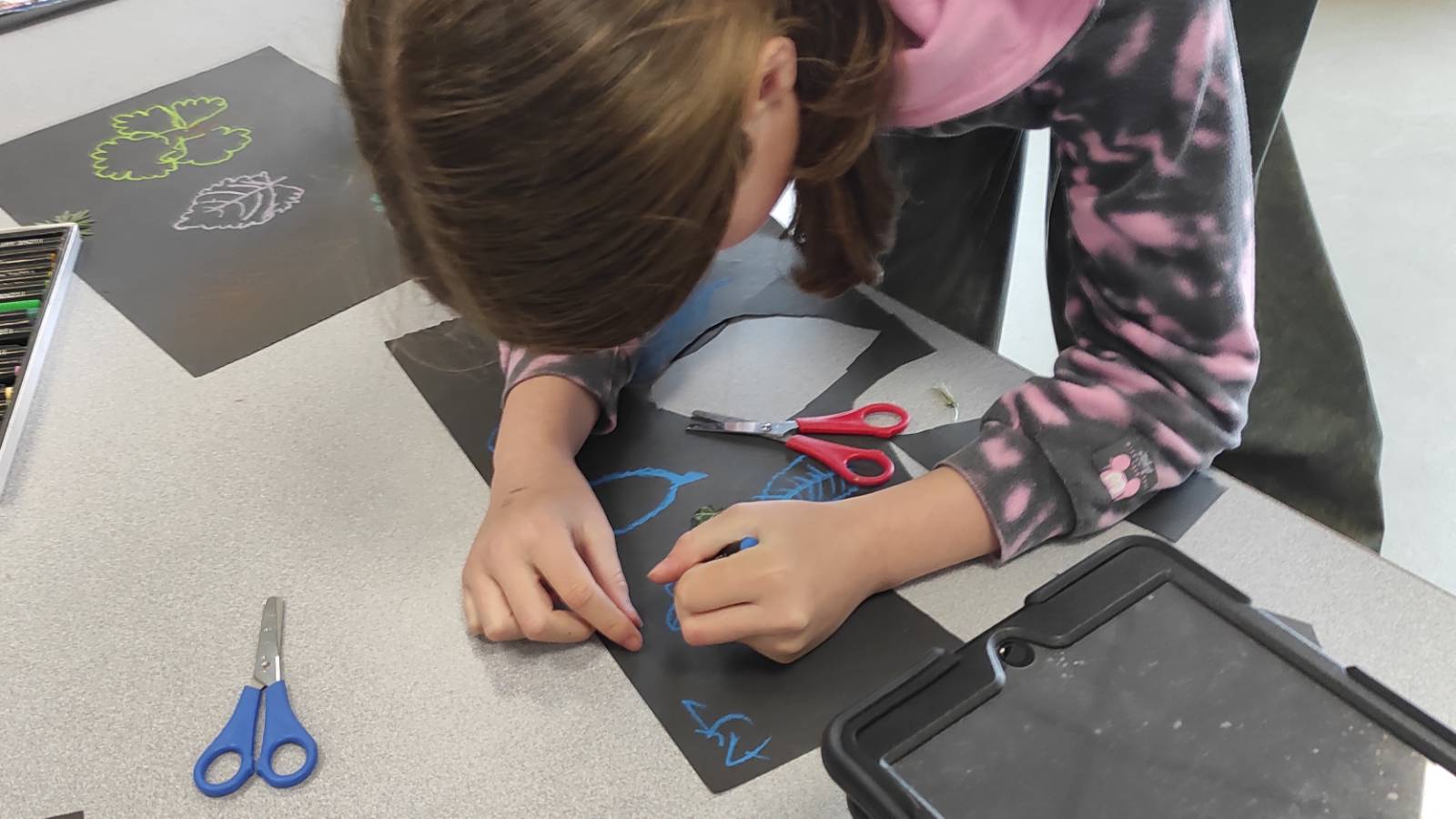 Student drawing leaves on black paper and cutting out shapes