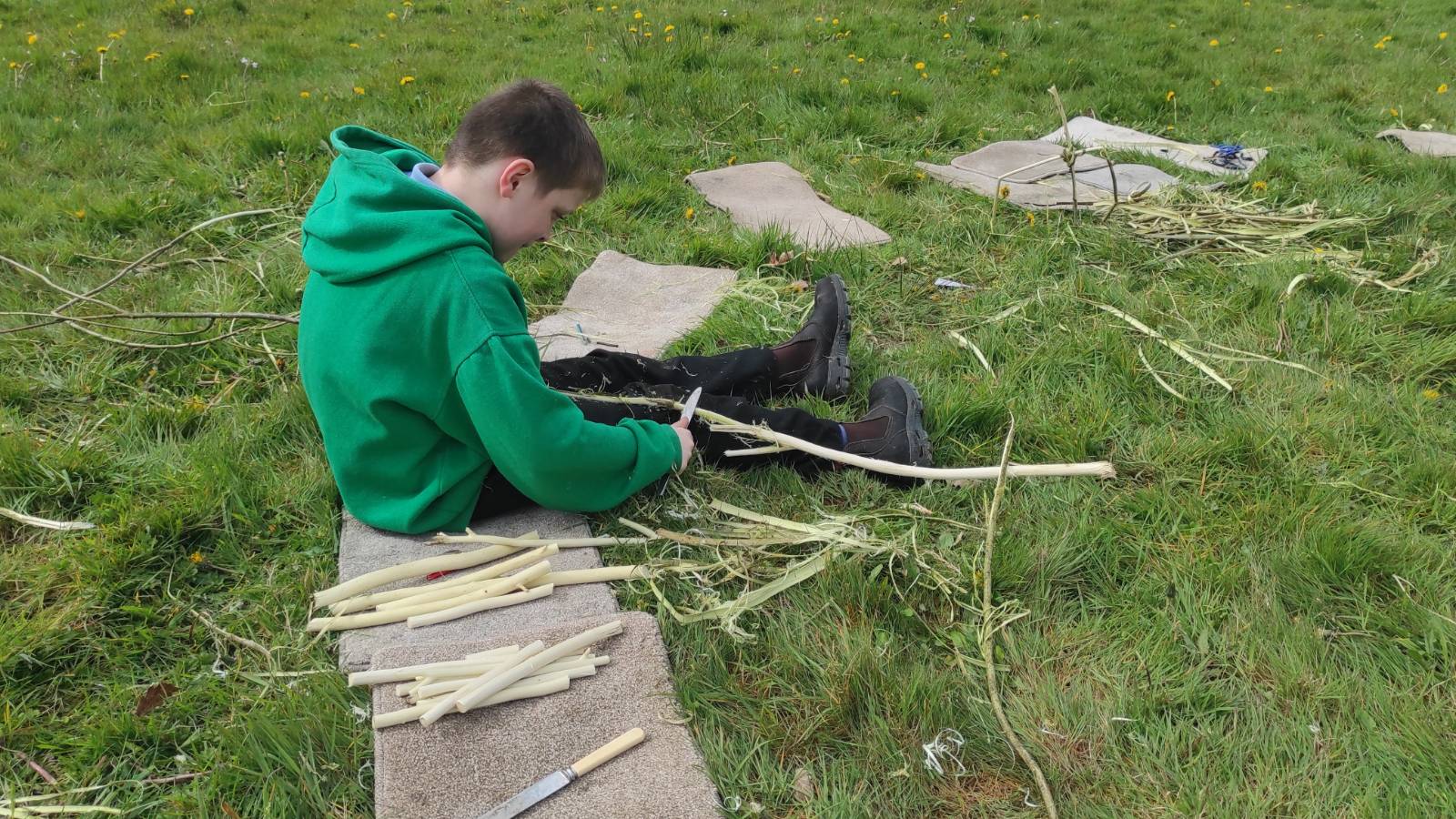 Student sat on carpet map stripping a big pile of willow sticks.
